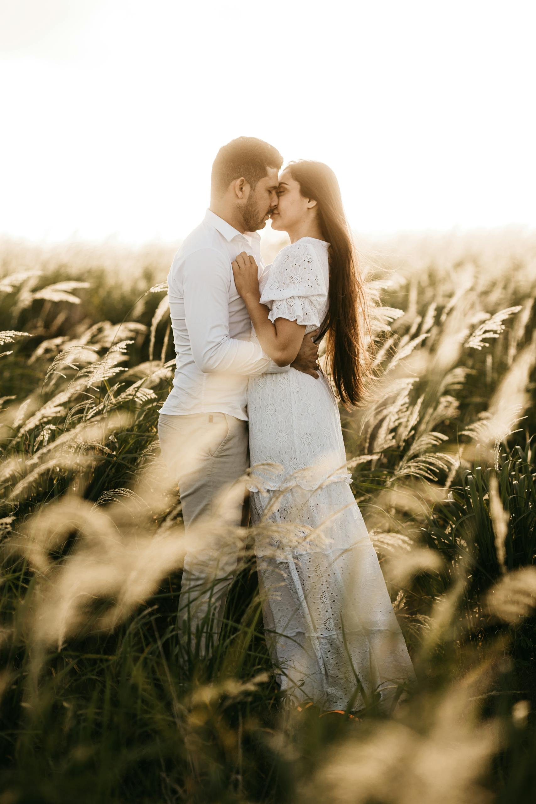 A loving couple in a white dress and shirt embracing in a sunlit field.